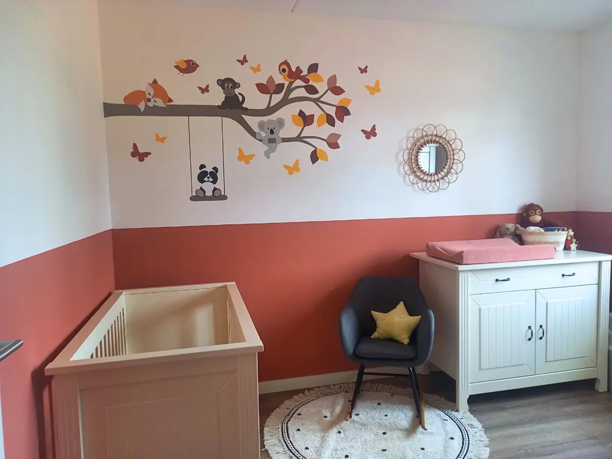 Terracotta babykamer met een behangsticker van een tak met vrolijke dieren in oker, roest, terracotta